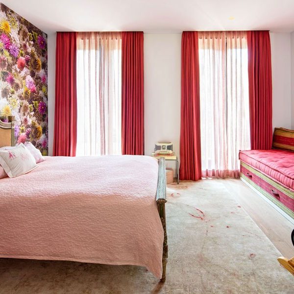 A cama antiga e o rosa suave da colcha sobre a cama suavizam a força do papel de parede no quarto da filha da designer.