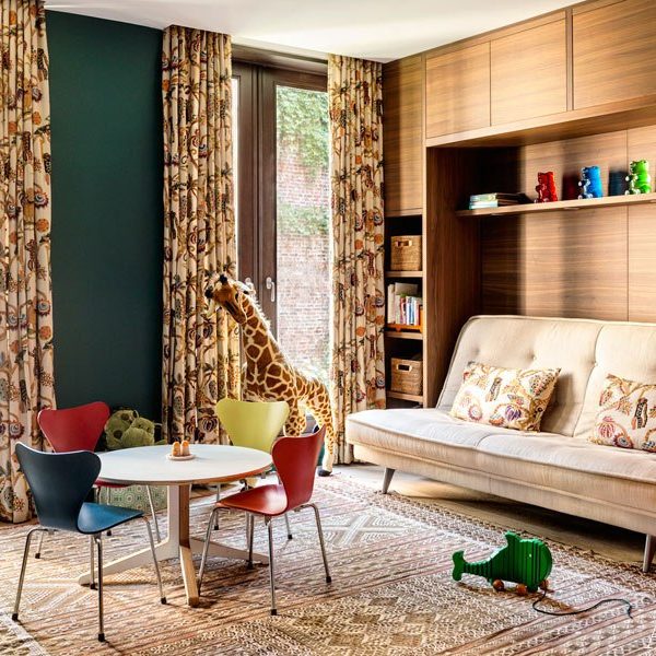 Na sala de brinquedos, cortina com tecido Clarence House, sofá Ligne Roset e cadeiras coloridas Arne Jacobsen. A parede verde dá um ar de floresta bem bacana!