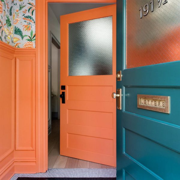 O hall de entrada, em laranja com tapete em pastilhas, recebe papel de parede Osborne & Little estampado. Charme puro!