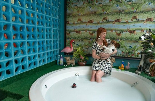 A banheira de hidromassagem fica em um deque revestido de grama sintética, com parede de cobogós e, ao fundo, uma toalha plástica de mesa que virou quadro na parede.
